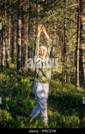 Donna che cammina attraverso una foresta di pini autunnale, respira l'aria del bosco e solleva entrambe le mani insieme Foto Stock