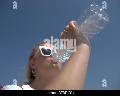 Donna che finisce una bottiglia d'acqua al sole Foto Stock