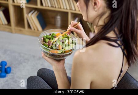 Donna in forma che mangia insalata fresca dopo l'allenamento a casa, concetto di dieta e nutrizione sana Foto Stock