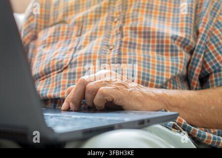 Prima di mani di un uomo anziano che digita su un laptop. Un uomo anziano è seduto sul divano mentre digita su un laptop. Concetto di tecnologia e persone anziane. Foto Stock