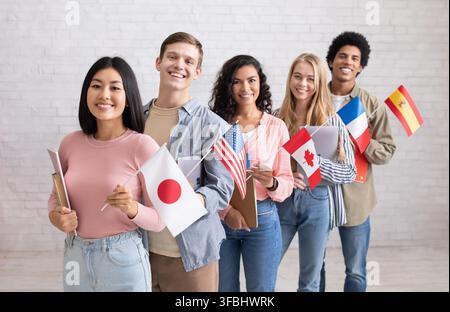Scambio internazionale di studenti multietnici. I giovani allegri con dispositivi e libri guardano alla macchina fotografica Foto Stock