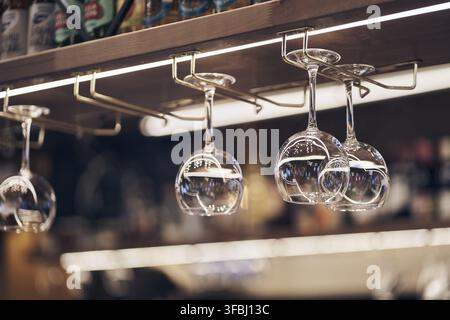 Primo piano di bicchieri da vino trasparenti vuoti capovolti sospesi su scaffali di legno dritti. Con spazio per copiare. Foto Stock