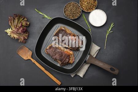 due pezzi di manzo fritti sono in una padella su un tavolo nero, accanto alle spezie, il grado di preparazione del piatto è ben fatto Foto Stock