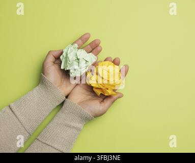 le mani femminili tengono un foglio di carta verde e giallo sbriciolato su uno sfondo verde, vista dall'alto Foto Stock