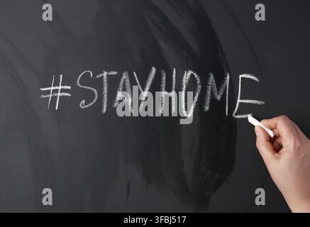 iscrizione rimanere a casa in gesso con un hashtag su una lavagna nera, concetto di auto-isolamento in un'epidemia e pandemica Foto Stock