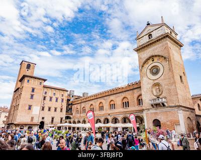 Mantova, Italia - 2025.04.26: Folle di persone che si radunano in Piazza delle Erbe a Mantova, godendosi l'architettura intorno alla storica Torre dell'Orol Foto Stock