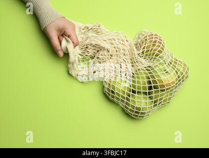 borsa in tessuto beige a mano con mele verdi su sfondo verde, il concetto di oggetti riutilizzabili, zero rifiuti Foto Stock