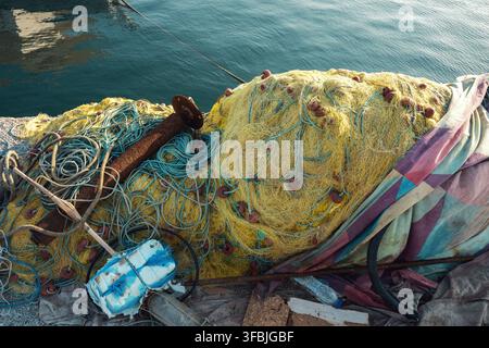 Reti da pesca gialle e blu impilate con galleggianti e corde appoggiate su un molo di cemento del porto vicino al mare, Grecia. Foto Stock
