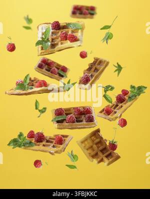 I waffle belgi al forno, i lamponi e le foglie di menta si levitano su sfondo giallo Foto Stock