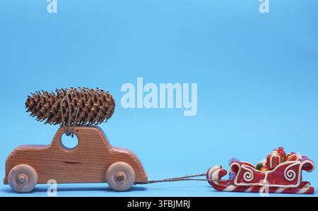 Macchina giocattolo di legno con una pigna sopra su uno sfondo blu, sfondo natalizio Foto Stock