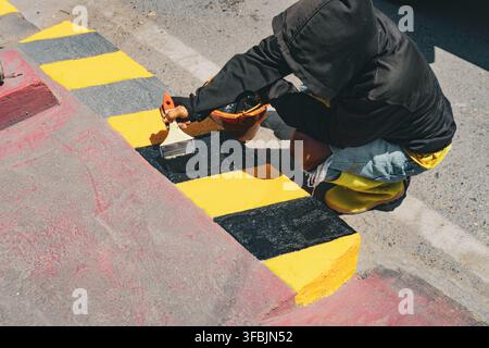 Lavoratore che dipinge segnaletica nera e gialla su un marciapiede di cemento a Luwuk, Banggai, Indonesia. Foto Stock