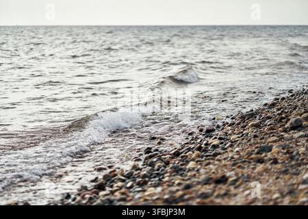 Piccole onde gentili che si infrangono su una riva ghiaiosa colorata con acqua limpida che increspa su pietre lisce lungo la costa della Grecia. Foto Stock