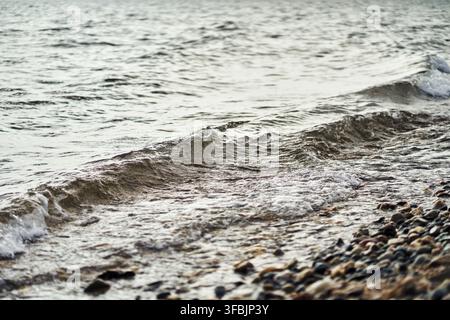 Piccole onde gentili che si infrangono su una spiaggia di ciottoli rocciosi sulla costa con acqua limpida e texture naturali, Grecia. Foto Stock