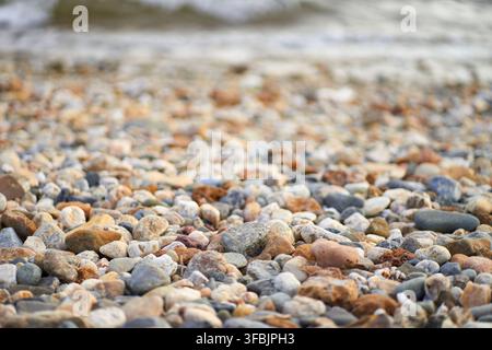 Prima vista di una raccolta diversificata di ciottoli lisci e pietre levigate colorate sparse lungo una riva naturale con onde gentili del mare Foto Stock