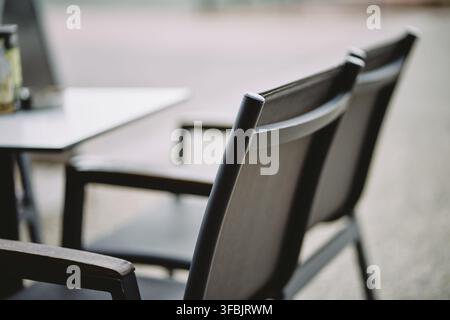 Vista ravvicinata di sedie moderne vuote da caffè e di un tavolo sistemato su una terrazza all'aperto, che mostra un design di mobili contemporaneo. Foto Stock