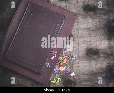 Due libri in rosso copre su un di legno marrone, sfondo dalla caduta di libri lettere multicolori, vista dall'alto, lo spazio vuoto sulla destra Foto Stock
