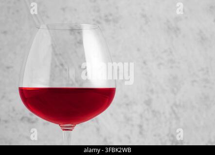 Vino rosso che riempie un grande bicchiere, presentando un concetto di bevanda minimalista ed elegante su uno sfondo grigio testurizzato Foto Stock