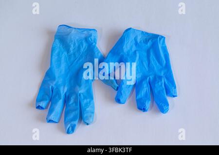 Due guanti medici monouso in lattice blu usati sono disposti ordinatamente su una superficie bianca semplice e pulita. Foto Stock