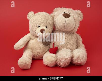 due orsacchiotti beige seduti accoccolati insieme, giocattoli su sfondo rosso, concetto di amicizia e amore Foto Stock