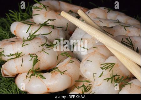 Prima vista di gamberetti sbucciati appena cotti e bacchette su sfondo scuro Foto Stock