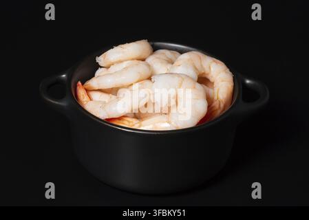 Il contrasto di visualizzazione cucinati freschi sbucciati gamberi o gamberetti in recipiente scuro su sfondo nero Foto Stock