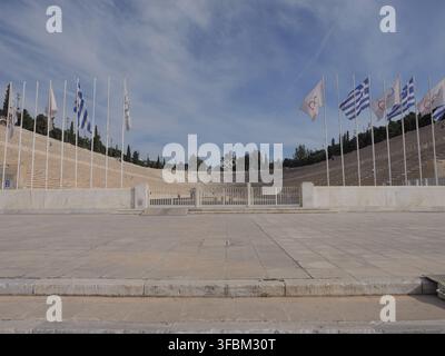 Vista dello storico Stadio Panatenaico con i suoi iconici gradini di marmo, gli anelli olimpici e le file di bandiere sotto un cielo blu limpido ad Atene, Grecia. Foto Stock