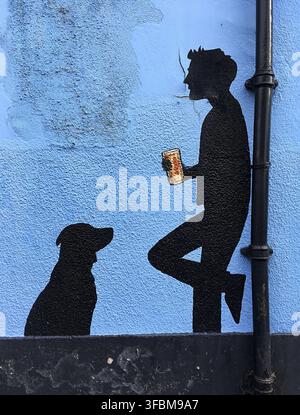 Prima piano di un murale di un uomo che beve birra con il suo cane in nero su una parete blu. Foto Stock