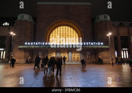 Helsinki, Finlandia-30 nov. 2025: Vista frontale notturna dell’ingresso illuminato della Stazione Centrale di Helsinki con pedoni. Foto Stock