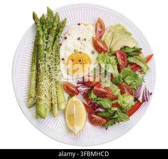 Piatto rotondo con asparagi cotti, uova fritte, avocado e insalata di verdure fresche, vista dall'alto Foto Stock