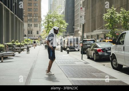 New York City, New York, USA - 07.30.2024: Un uomo si trova all'ombra con un asciugamano sulla testa per proteggersi dal caldo a New York City. La b Foto Stock