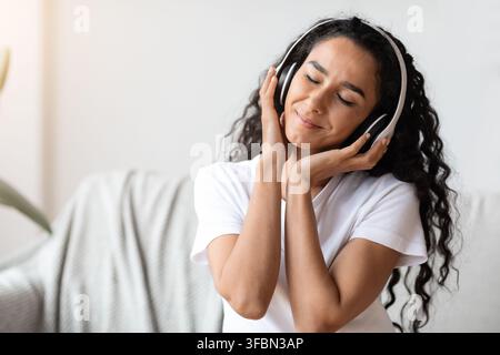 Giovane donna emozionale con cuffie wireless che ascolta la musica Foto Stock