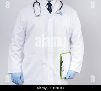 medico maschile in un cappotto bianco, guanti in lattice blu, uno stetoscopio appeso al collo, medico che tiene un porta-carta verde con un foglio bianco vuoto Foto Stock