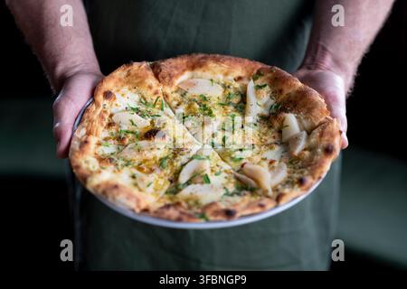 Deliziosa pizza ricoperta di pere fresche ed erbe, servita con cura Foto Stock