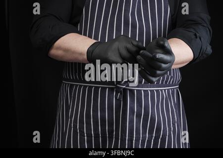 chef uomo in uniforme nera e grembiule a righe abiti guanti in lattice, low key Foto Stock