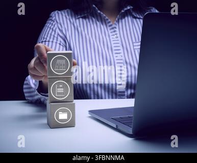 Una donna è seduta a un tavolo con un laptop e tiene dei cubi di legno con icone. Il concetto di controllo dei processi aziendali Foto Stock