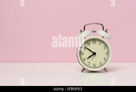 sveglia in metallo bianco su un tavolo bianco, dalle dieci alle otto del mattino, spazio copia Foto Stock