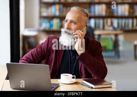Un uomo d'affari anziano occupato che parla al telefono al caffè Foto Stock