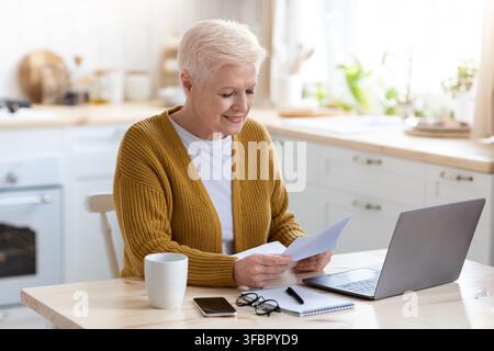 Nonna felice seduta in cucina, leggendo la lettera Foto Stock