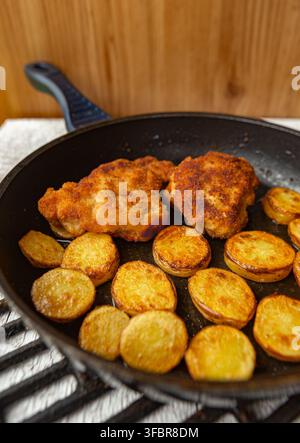 Schnitzel di pollo impanato con fette di patate arrosto in padella Foto Stock