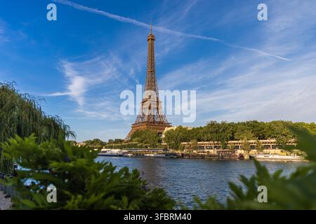 PARIGI, FRANCIA - 20 LUGLIO 2026: La Torre Eiffel incorniciata da una lussureggiante vegetazione sul lato opposto della Senna a Parigi. Foto Stock
