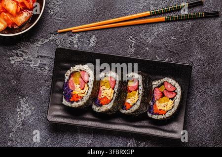 Un piatto nero pieno di kimbap (o gimbap) con ripieni colorati. Gli ingredienti includono salsiccia, cetrioli, uovo e verdure. Foto Stock