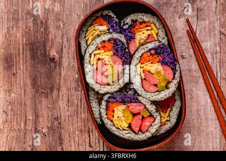 Kimbap (o gimbap) colorato con verdure e salsiccia in una scatola di legno su una superficie di legno Foto Stock