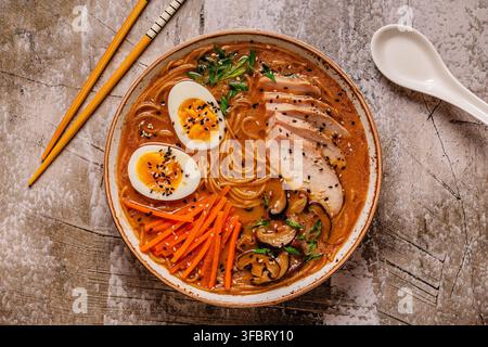 Ciotola di ramen con pollo, uova e verdure pronta da mangiare su un tavolo strutturato Foto Stock