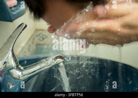 Un uomo si lava il viso con le mani sopra un lavandino in bagno Foto Stock