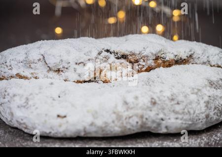Un primo piano di un tradizionale panettone natalizio con frutta generosamente cosparso di zucchero a velo che cade su uno sfondo scuro con Foto Stock