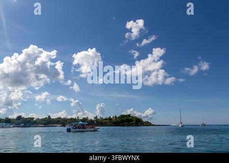 Mare blu calmo con piccole barche vicino alla costa di un'isola tropicale sotto un cielo blu profondo pieno di nuvole bianche brillanti. Foto Stock