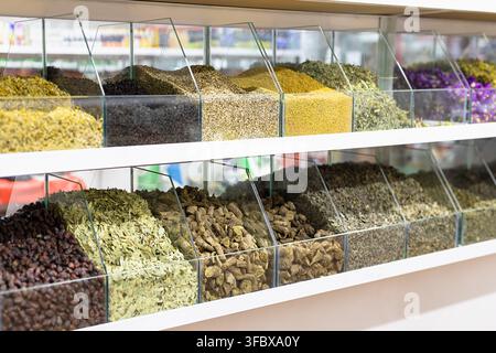 Spezie ed erbe essiccate esposte in scomparti di vetro in un bazar a Bukhara, Uzbekistan. Varietà di condimenti colorati macinati, radici e fiori essiccati Foto Stock