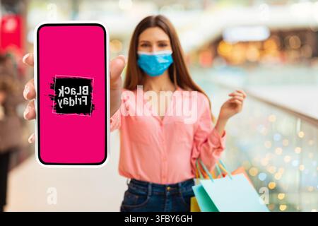 Donna che tiene uno smartphone con promozione Black Friday, ambientato in un centro commerciale Foto Stock