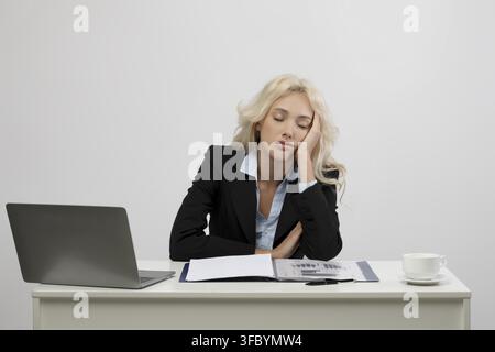 Giovane donna annoiata con lunghi capelli seduta alla scrivania in ufficio con laptop, concetto aziendale Foto Stock
