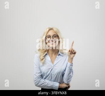 Giovane donna caucasica sorridente che punta verso l'alto con il dito, espressione gioiosa, concetto di studio Foto Stock